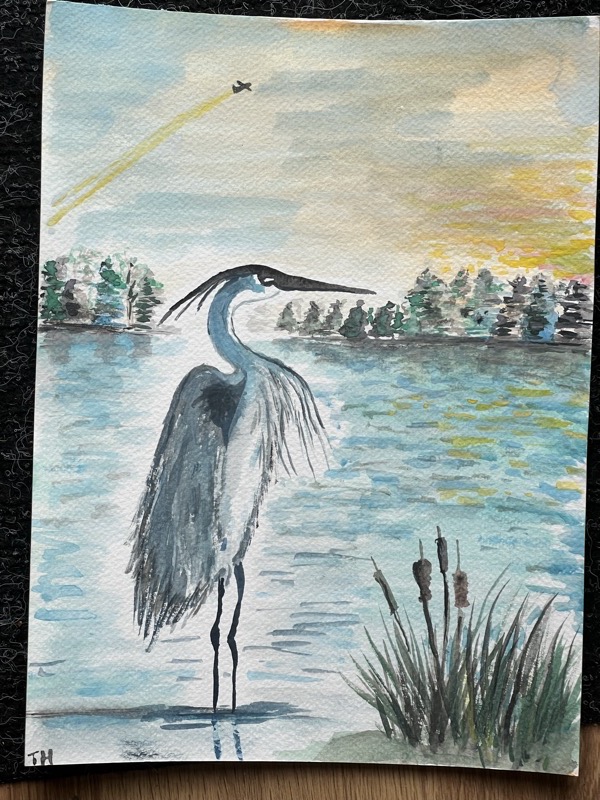 Watercolour of a heron standing in the shallows at the edge of a lake, a dark treeline and a yellow-lit sky behind.